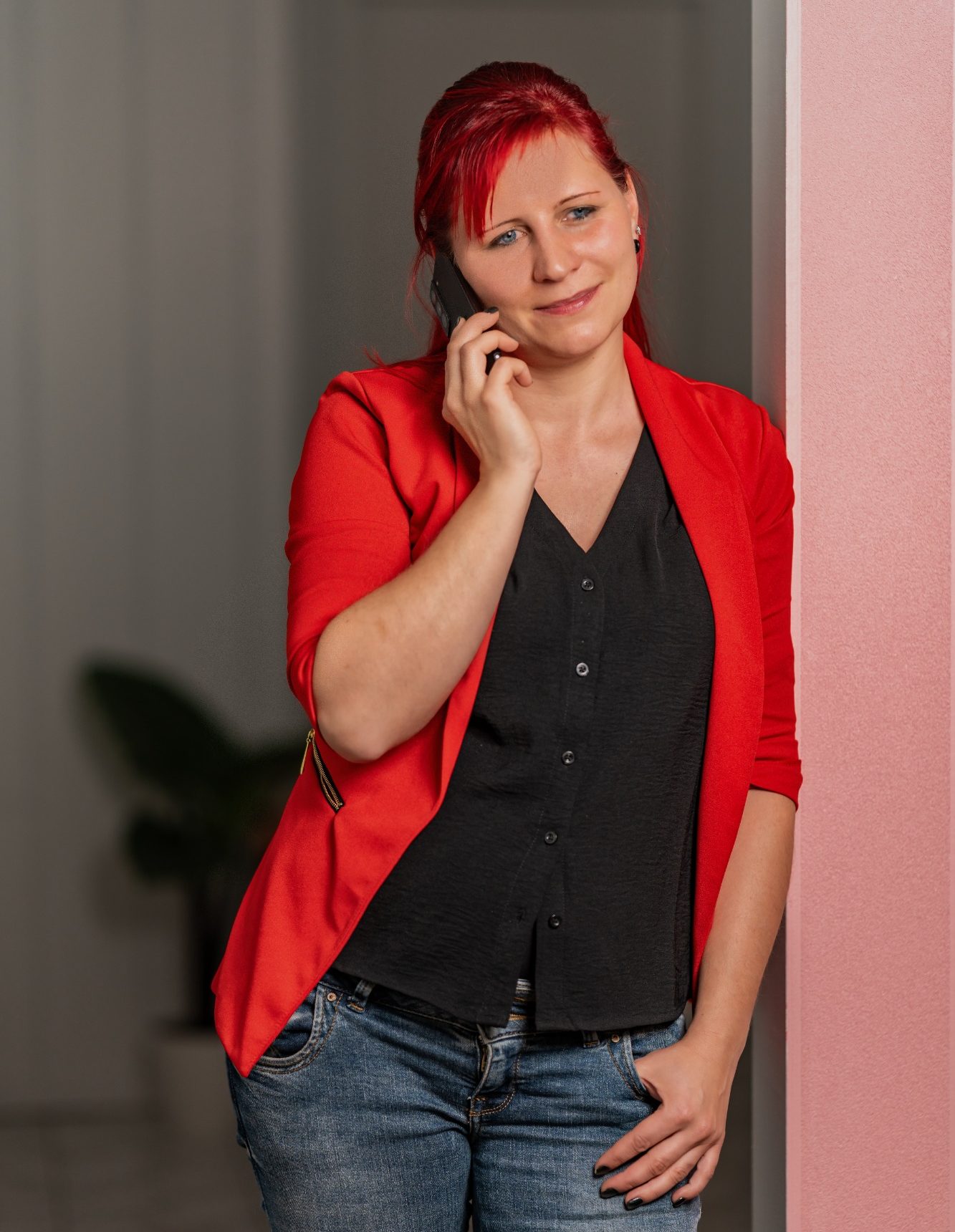 Buche deine Transformation Frau mit rotem Blazer und schwarzem Oberteil, die am Telefon lächelt.