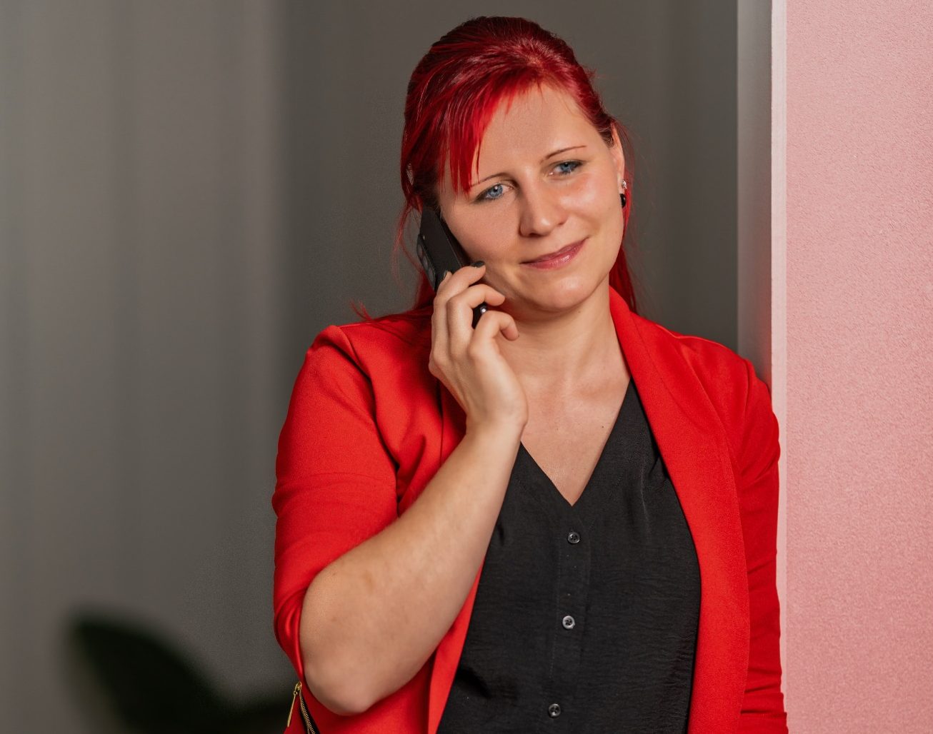 Kostenloses Gespräch buchen Frau mit roten Haaren und rotem Blazer, die ein Tablet in der Hand hält.