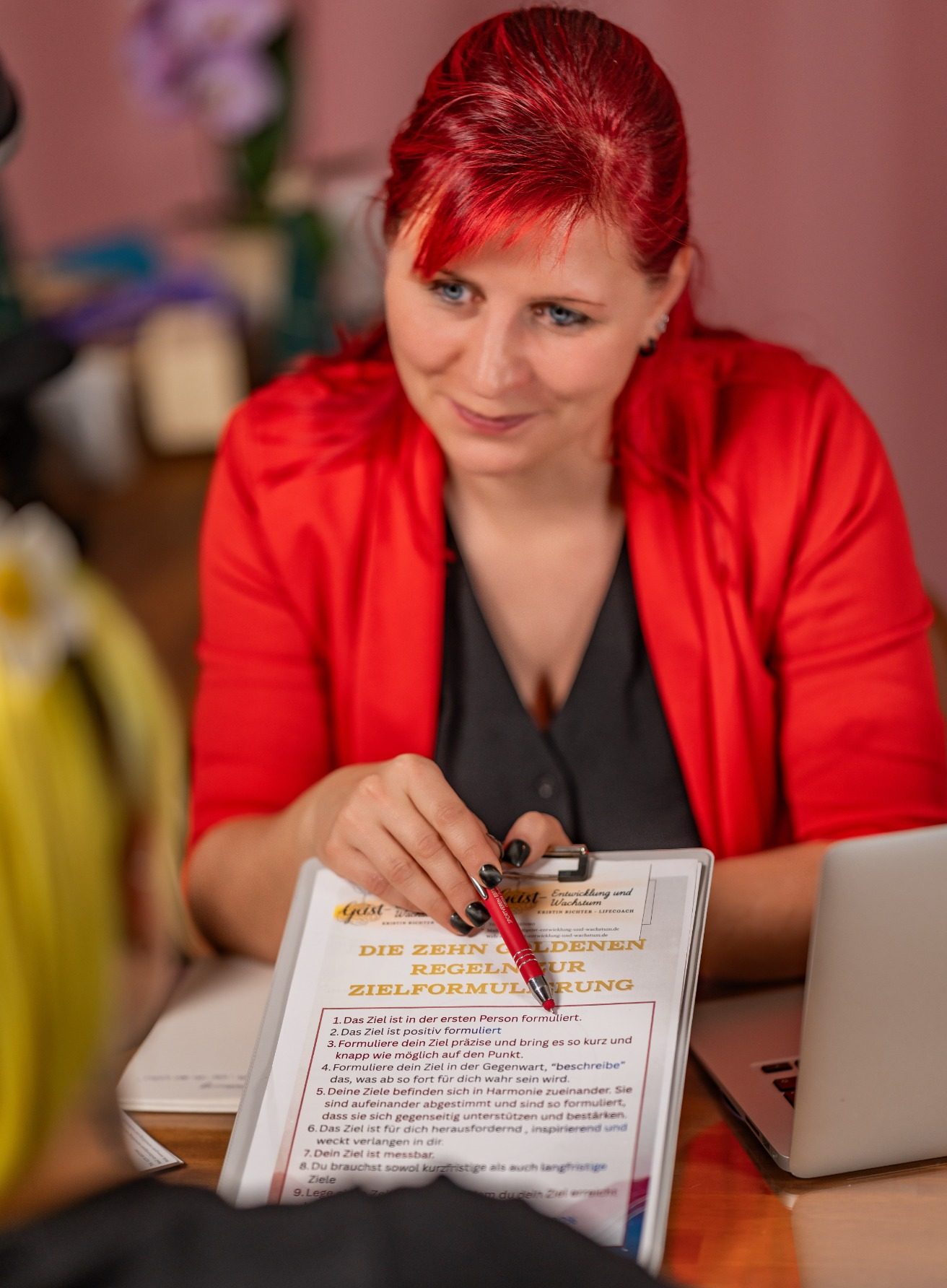 Deine Transformation Eine Person mit rotem Blazer hält ein Notizbuch und einen Stift in der Hand.